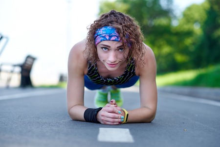 Attractive young woman athlete doing plank exercise on stadiumの写真素材
