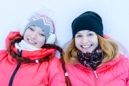 Two young happy smiling girl lying on the snow in winter park. Outdoor portraitの写真素材
