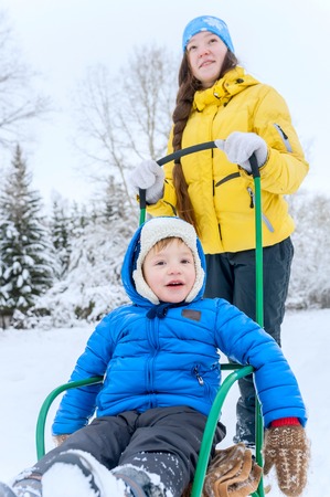Outdoor portrait  Mom walks with the son in the winter. She carries it on a sled through the snow