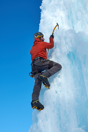 Alpinist man with ice tools axe climbing a large wall of ice. Outdoor Sports Portraitの写真素材