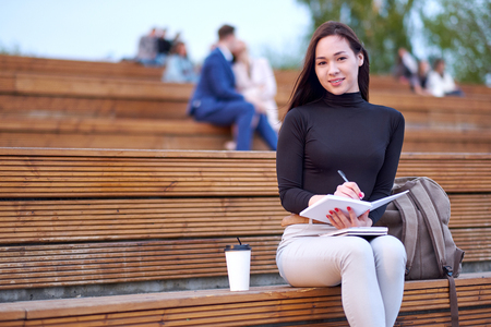 Young asian woman with pen writing in notepad. outdoor city portrait.の写真素材