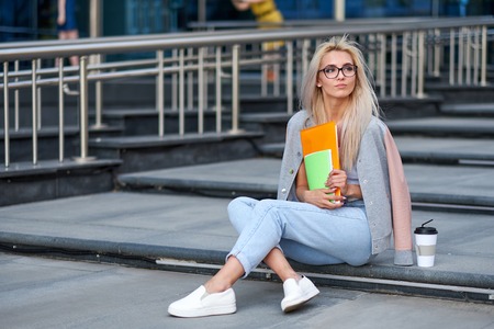 Young beautiful student woman writing and reading book on stairs of university or college, preparing for exams. Education concept, copy space.の写真素材