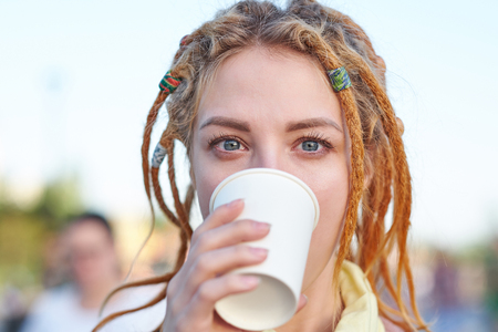 Portrait young woman with dreadlocks drinking coffee in paper cupの写真素材