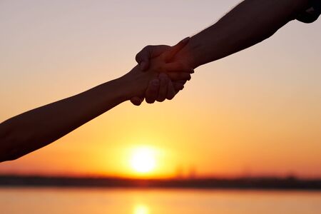Giving a helping hand.Two hands, man and woman, holding tight at sky sunset.の写真素材