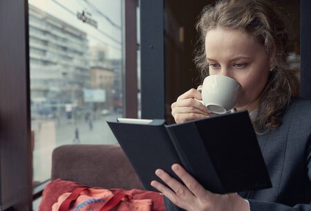 Young woman in a restaurant reading a book and drinking coffee