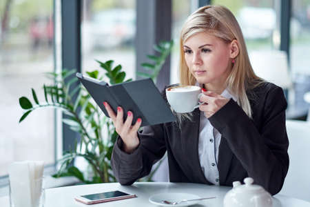 Young woman in cafe reading an ebook and drinking coffee.の写真素材