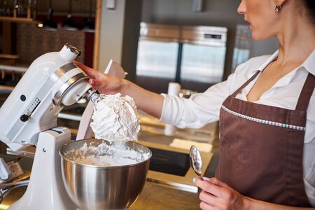 Woman using mixer standing at counter in her apron. Making dessert in pastryの写真素材