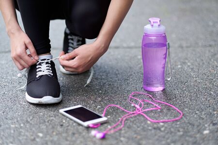 runner woman tying running shoes laces getting ready for race on run track stadium with bottle of water and phone with headphonesの写真素材