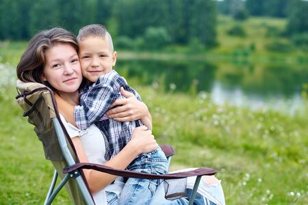 Mother and son sitting on chair and relaxing in nature near the lake. Outdoor activity in summer. Adventure traveling in national park. leisure, vacation, relaxationの写真素材