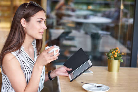 Young business woman in a cafe reading an ebook and drinking coffee