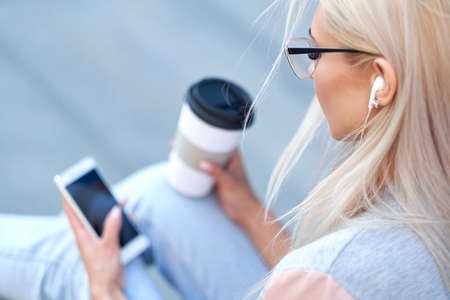 Beautiful woman using phone and drinking coffee on a city street