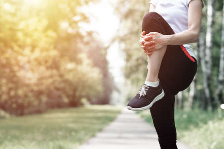young fitness woman runner stretching legs before run on grass.
