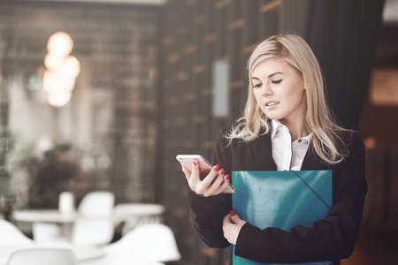 Young business woman writing a message on smart phone and smiling in officeの写真素材