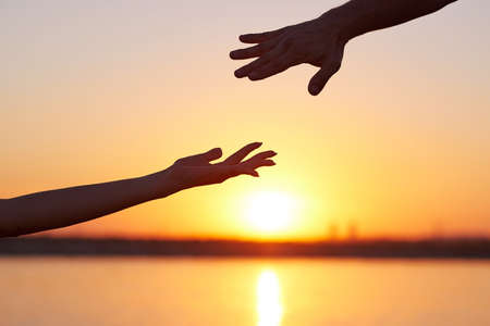 Giving a helping hand.Two hands, man and woman, reaching towards each other at sky sunset.の写真素材