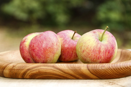 Three red ripe apples on wooden plate close-upの写真素材