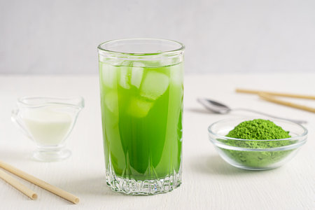 Organic homemade healthy matcha latte made of green tea leaves ground powder mixed with milk or water served in glass on white wooden table with paper straw for breakfastの写真素材