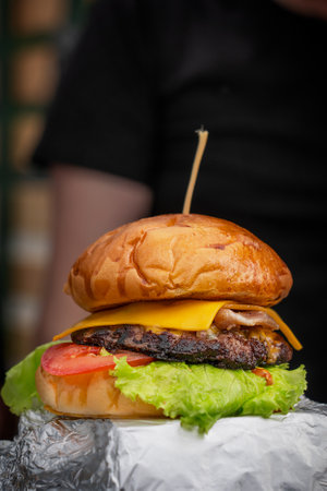 Tasty juicy burger or cheeseburger made of grilled beef meat, green lettuce, cheese and tomato slice between roasted bun bread served at barbeque street food festival at restaurantの写真素材