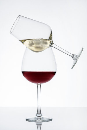 Two wineglasses on top of one another with red and white wine with ice cubes served on table with reflection against white background prepared for party celebrationの写真素材