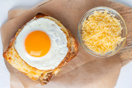 Close up top view of Croque Madame French baked homemade hot sandwich made of ham and cheese inside toasted bread topped with fried egg with yolk served on parchment paperの写真素材