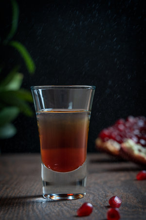Alcohol cocktail made of hard liquor mixed with Grenadine nonalcoholic bar syrup of deep red color made from pomegranate served in shot glass on brown wooden tableの写真素材