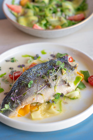 Roasted cooked half of fish decorated by chef with cherry tomatoes, cucumber slices, microgreen and...