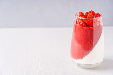 Homemade sweet healthy panna cotta italian organic dessert made of layer of cream with gelatine and strawberry sauce with topping of chopped berries in glass on white wooden tableの写真素材