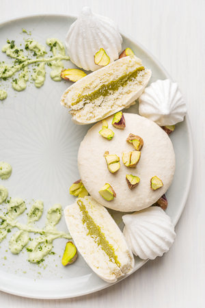 Top view of sweet macaron or French macaroon meringue-based confection dessert with pistachio flavor buttercream decorated with crushed nuts and cream cheese served on plateの写真素材