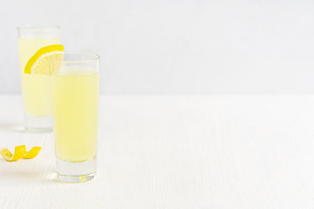 Italian Limoncello homemade natural liqueur made from the zest of ripe yellow lemons served chilled as an digestif or aperitif in glass shot on white wooden table with copy spaceの写真素材