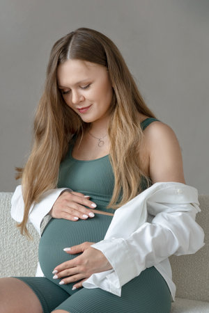 Close up portrait of beautiful sporty pregnant young woman with long blonde hair wearing sportswear and shirt smiling and resting in anticipation of happy motherhood, lookingの写真素材