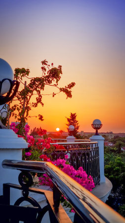 Beautiful colorful sunset on outside balcony with railings decorated with lanterns and plant with bright pink flowers with a view on amazing orange sun and dark blue skyの写真素材