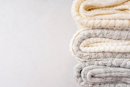 Close up view of stack of folded soft comfortable warm casual woven sweaters or cardigans knitted from white and gray wool or merino yarn against concrete wall with copy spaceの写真素材