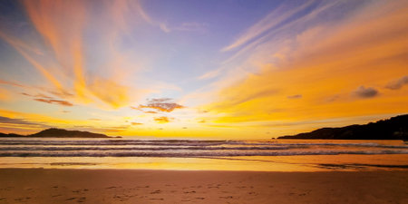 Beautiful peaceful tropical landscape with bright orange sunset at sandy seaside beach, sea water waves and sky with colorful clouds at scenic tranquil tourist destinationの写真素材