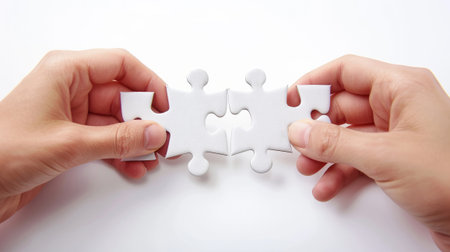 Close-up of hands holding and connecting two white puzzle pieces on a white background. Concept of teamwork, problem-solving, and partnershipの素材