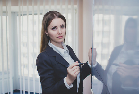 Businesswoman wearing grey suit standing near whiteboard holding markerの写真素材