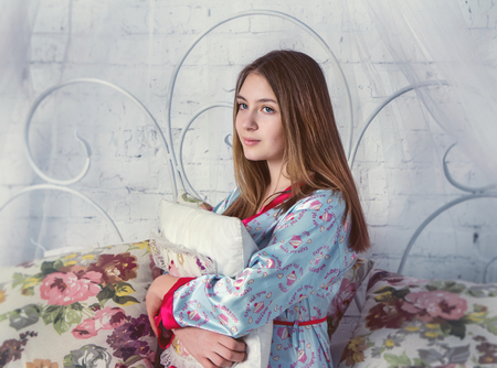 Teen girl sitting on a bed in her bedroom holding pillowの写真素材