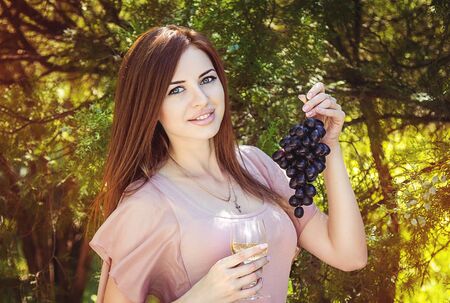 Beautiful young smiling woman in pink dress  holding wineglass and black grapeの写真素材