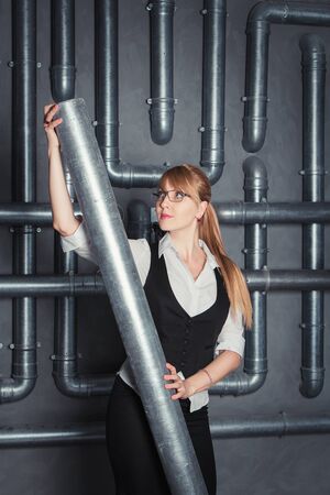 Attractive businesswoman wearing glasses holding PVC pipe  on a pipes backgroundの写真素材
