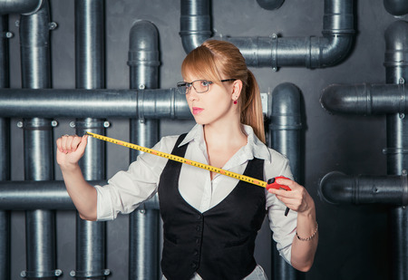Attractive businesswoman wearing glasses holding measure tape on PVC pipes backgroundの写真素材