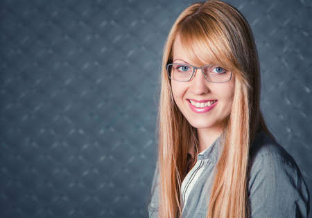Portrait of beautiful young smiling woman with blond long hair wearing glasses posing against chain link fenceの写真素材