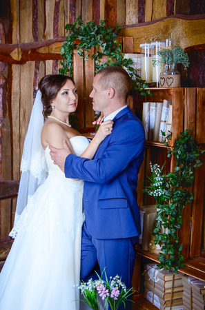 Studio portrait of bride and groom hugging in a room with wooden walls and book shelves on their wedding day, vintage interiorの写真素材