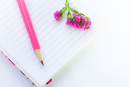 empty note book, pink pencil and flower on a white textile background