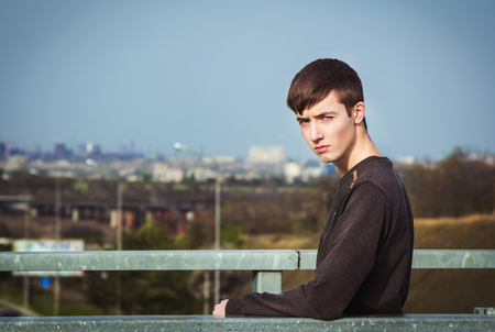Portrait of sad and gloomy frowning young man standing on the bridge under city roadの写真素材
