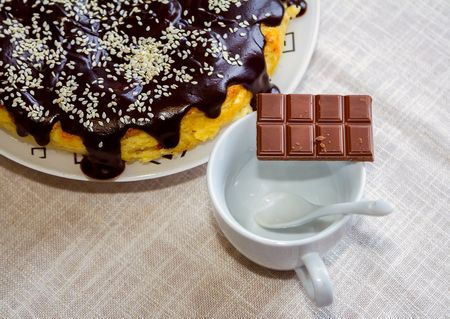 Cheesecake with chocolate glaze and sesame, bar of milk chocolate on a white empty coffee cup