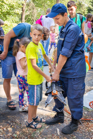 Zaporizhia/Ukraine- September  3, 2016: Charity festival for children â City of professions . Rescue service volunteer demonstrates hydraulic rescue equipment â spreader to  teen boy.のeditorial素材