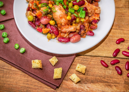Homemade Stewed beans with chicken meat green peas and vegetables served with cut green onion and parsley on a white plate and croutons on wooden tableの写真素材