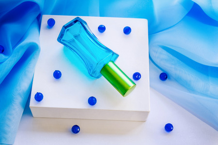 Blue glass perfume bottle on a white box with beads and textileの写真素材