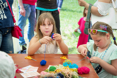 Zaporizhia / Ukraine- May 28, 2017: Charity Family Festival- girls learning to make colorful table napkins at knitting workshop, outdoors children activityのeditorial素材