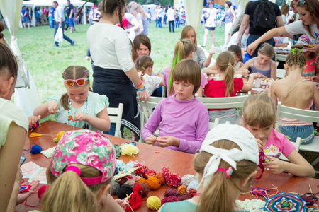 Zaporizhia / Ukraine- May 28, 2017: Charity Family Festival- girls and boys learning to make colorful table napkins at knitting workshop, outdoors children activityのeditorial素材