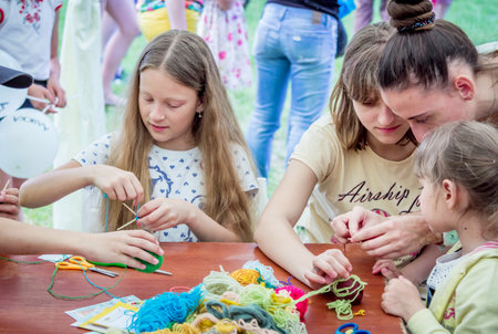 Zaporizhia / Ukraine- May 28, 2017: Charity Family Festival- girls learning to make colorful table napkins at knitting workshop, outdoors children activityのeditorial素材