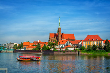 Wroclaw / Poland-August 18, 2017: View of the Church of the Holy Cross and St. Bartholomew on Tumski Island, Odra river with touristic boat, blue sky, summer.のeditorial素材